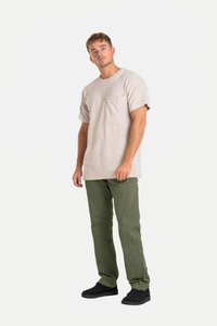 Beige T-Shirt mit kurzen Ärmeln und Brusttasche, kombiniert mit grünen Hosen und schwarzen Schuhen, vor einem schlichten weißen Hintergrund.