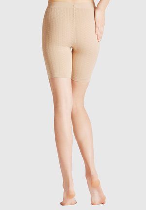 Rückenansicht einer Person, die beige strukturierte knielange nahtlose Shorts trägt und auf den Zehenspitzen steht, mit einer Hand auf der Hüfte.