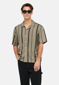 Short-sleeve shirt in light olive green with vertical black stripes, collared design, and white buttons. Paired with black pants.