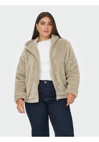 Hoodie z futra w odcieniach beżu, z zamkiem z przodu, kapturem ze sznurkiem i ściągaczami, w połączeniu z ciemnoniebieskimi dżinsami o podwyższonym stanie.