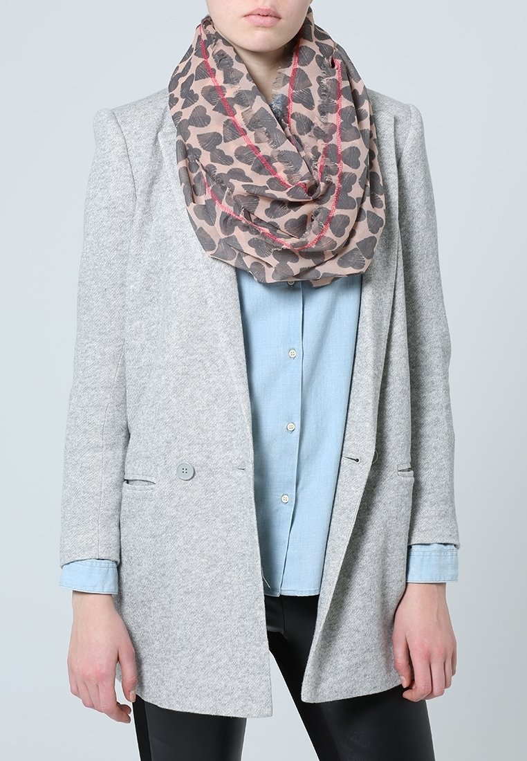 Personne portant un blazer gris clair sur une chemise bleue boutonnée et un pantalon noir, accessoirisée avec une écharpe rose et noire à motifs de cœurs.