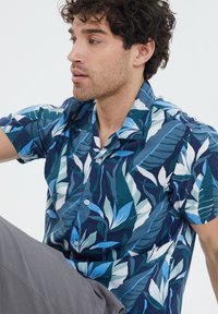 Korte mouwen overhemd met een blauw en groen bladerenpatroon op een donkere achtergrond. De stof lijkt soepel met een ontspannen pasvorm.