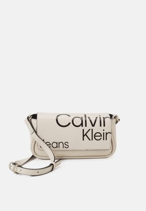 Petit sac bandoulière Calvin Klein écru avec bandoulière ajustable et grand texte de logo noir sur le rabat avant.