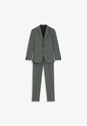 Szary garnitur w kratę z jednorzędową marynarką, klapami w szpic i dwoma przednimi kieszeniami; spodnie o prostych nogawkach z podwiniętymi mankietami.