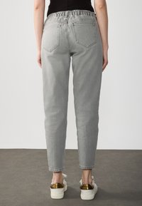 Pantalones de mezclilla gris con cinturilla elástica, diseño de cinco bolsillos y pierna ajustada. Llevados con zapatos blancos con detalles en dorado.