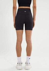 Zwarte high-waisted shorts van rekbaar materiaal, met een gladde textuur en een logo-accent op de achterkant, die halverwege de dij eindigen.