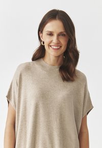 Beżowy, oversize'owy sweter dzianinowy z krótkimi rękawami i wysokim kołnierzem, charakteryzujący się gładką fakturą i minimalnym zdobieniem.