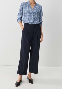 Blå mönstrad blus med V-ringning och långa ärmar. Vida marinblå byxor med framfåll och manschetter. Svarta spetsiga ballerinaskor.