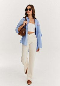 Niebieska i biała, w paski koszula, biały crop top, beżowe szerokie spodnie, brązowa torebka, brązowe sandały, okrągłe okulary przeciwsłoneczne, swobodny strój.
