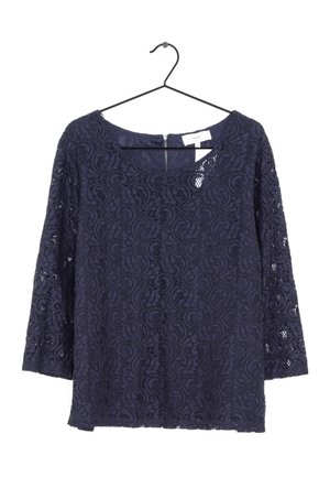 Blouse en dentelle bleu marine à manches longues avec un col rond suspendue sur un cintre noir.