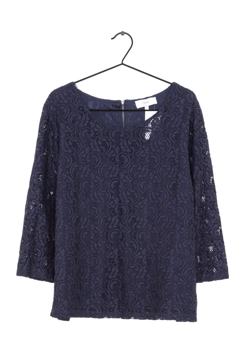 Blouse en dentelle bleu marine à manches longues avec un col rond suspendue sur un cintre noir.