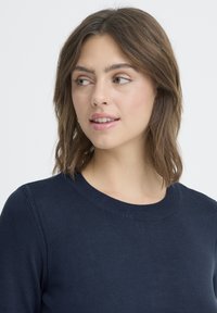 Tengerészkék pulóver kerek nyakkivágással és hosszú ujjakkal, sima kötött anyagból készült. Nincsenek látható minták vagy fém részletek.