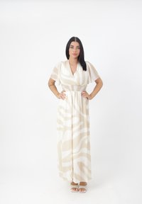 Robe maxi crème avec des motifs abstraits beiges, manches courtes à volants et taille smocks. Associée à des sandales de couleur claire.