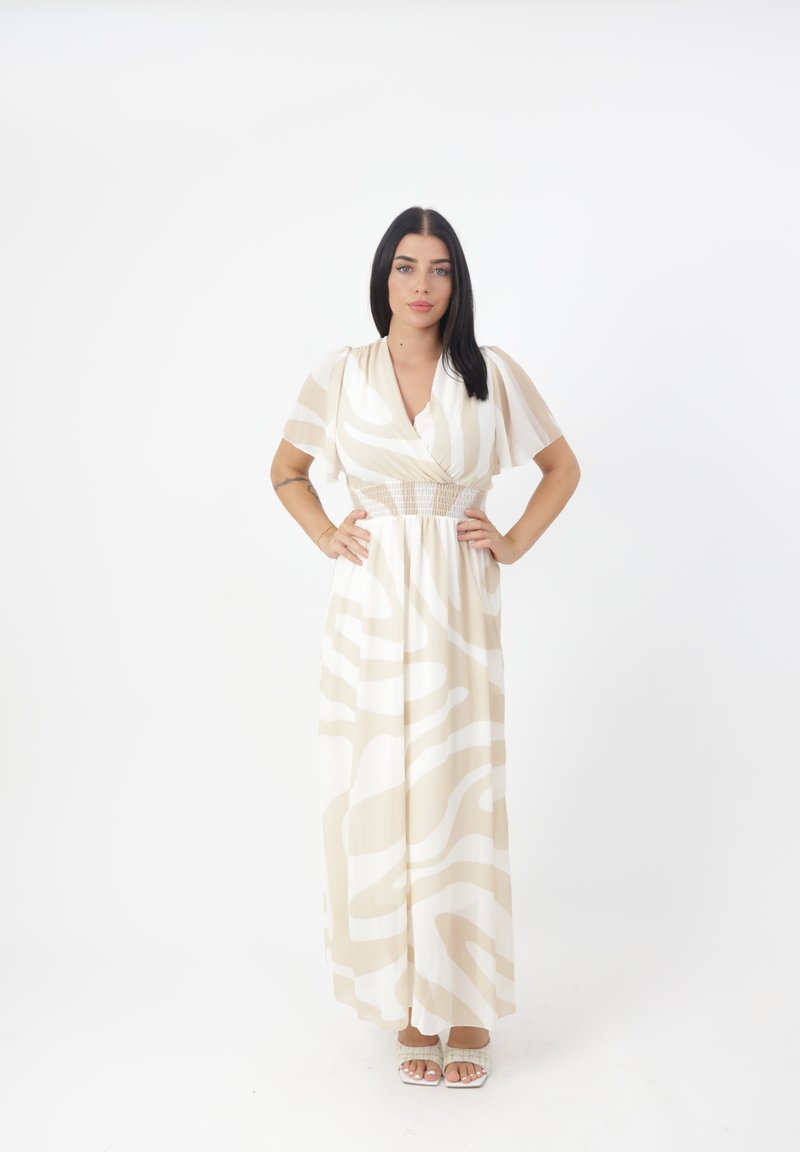 Robe maxi crème avec des motifs abstraits beiges, manches courtes à volants et taille smocks. Associée à des sandales de couleur claire.