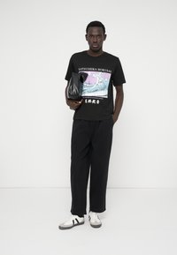 Μαύρο μπλουζάκι με γραφικό κύμα του Χοκουσάι; χαλαρές μαύρες παντελόνες; μαύρη τσάντα; γκρι και λευκά αθλητικά παπούτσια με μαύρες ρίγες; απλός και casual σχεδιασμός.