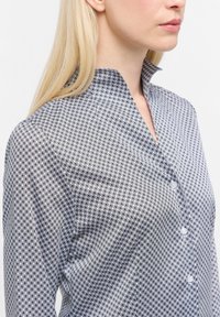 Camicia a maniche lunghe con bottone, in un motivo geometrico bianco e nero. Presenta un colletto alto e un tessuto leggero e liscio.