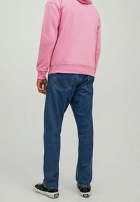 Rosa hoodie med ficka fram, parat med blå jeans och svart-vita sneakers. Avslappnad outfit med lös passform.