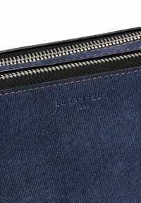 Portafoglio in denim con zip di colore blu scuro, con una superficie testurizzata, dotato di hardware metallico per la zip e stampa in rilievo del marchio sul davanti.