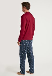 Maglietta rossa a maniche lunghe abbinata a pantaloni del pigiama blu navy con pois bianchi e motivi di ciliegie rosa. Il tessuto sembra morbido e leggero.