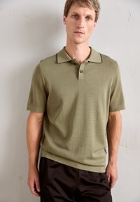 Khaki zielona koszulka polo z fakturowanym splotem, z dwoma guzikami zapinanymi, kontrastowym wykończeniem kołnierzyka i krótkimi rękawami, w zestawie z ciemnymi szortami.