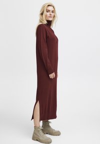 Burgundy långärmad klänning med mock neck, sidoflikar, texturerat stickat tyg, kombinerad med ljusbruna snörade ankle boots.