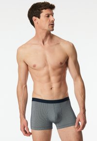 Boxers gris avec une texture côtelée, dotés d'une ceinture élastique bleue marine et de détails de logo. Design près du corps avec une coupe de jambe droite.