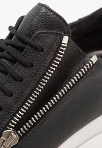 Černé kožené tenisky s výrazným kovovým zipem na boku, texturovaným povrchem a bílou gumovou podrážkou.