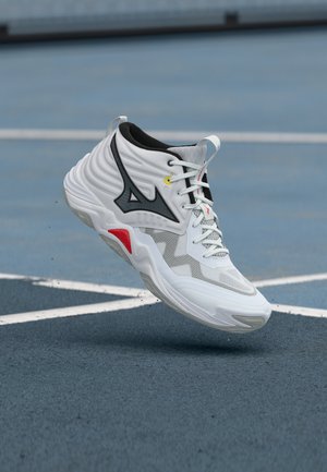 White high-top athletic shoe with black and red accents hovering above a blue sports court with white lines.
