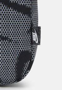 Černá a šedá texturovaná tkanina s pixelovaným vzorem, s malou bílou značkou loga Nike na boku.