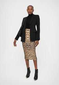 Črn krojen blazer preko črnega puloverja z visoko ovratnikom, v kombinaciji z krilom v leopardjem vzoru in črnimi gležnjarji. Gladke teksture in drzni vzorci.