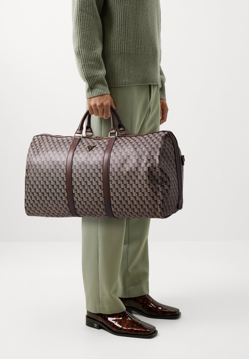 La borsa duffel tessuta presenta un motivo geometrico in tonalità di viola e marrone, con manici in pelle marrone scuro e dettagli in metallo dorato.