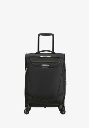 Valise cabine rigide noire American Tourister avec poignée télescopique et poche avant zippée, debout sur quatre roues pivotantes.