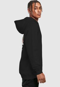 Svart hettegenser med en frontlomme og grafisk design på brystet. Stoffet ser mykt ut med en glatt tekstur og justerbar snor.