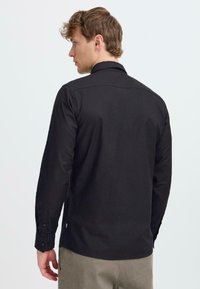 Black long-sleeve button-up shirt with a straight collar, features a smooth texture, and side slits. Buttons on cuffs, simple design.