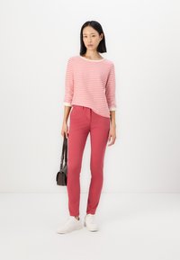Röd och vit randig långärmad tröja med rund halsringning, parat med slim-fit rosa byxor och vita sneakers, hållande en liten svart väska.
