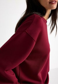 Bordeaux sweatshirt med en glat tekstur, rund halsudskæring og sænket skuldre, der har et minimalistisk design og subtile syninger.