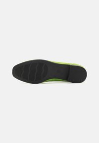 Zapato plano de ante verde con suela de goma negra que presenta ranuras horizontales para mayor agarre. El diseño es suave, con puntera redondeada y acentos mínimos.
