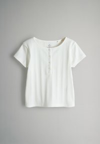 Haut blanc à manches courtes avec un col rond, présentant une texture côtelée verticale et quatre boutons sur le devant.