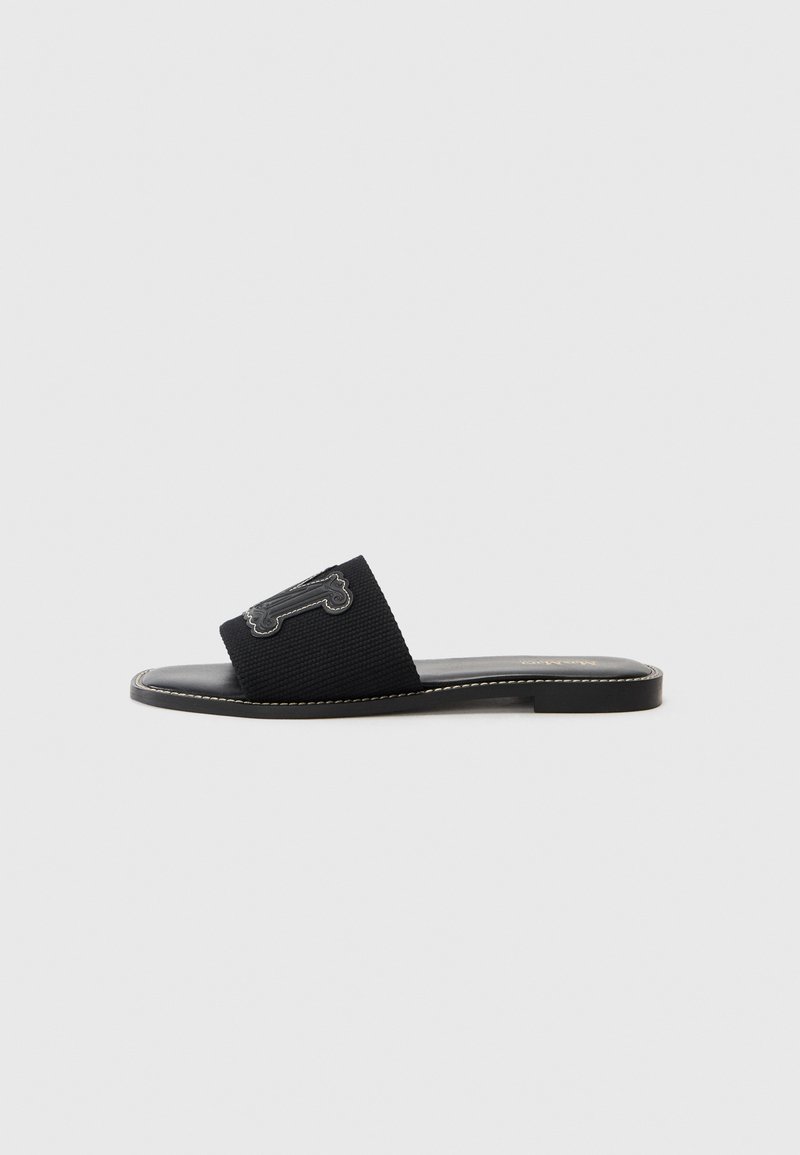 Sorte sklidesandal med teksturert overdel, med en beinformet detalj. Flat såle og kontrastsøm. Lett design.