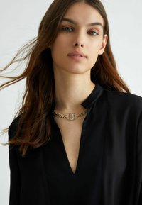 Blusa nera con scollo a V profondo, caratterizzata da un dettaglio colli con catena dorata. Tessuto morbido con un design minimalista.