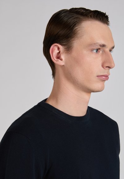 Navy blue crew neck sweater with a smooth texture, fitted design, and plain fabric, shown on a model from the side.