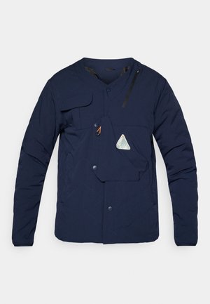 Tengerészkék steppelt dzseki V-nyakkal, nyomógombos záródással, elülső zsebbel és cipzáras díszítéssel, jellegzetes logóval és texturált anyaggal.