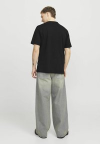 Sort bomulds t-shirt med korte ærmer, parret med lysegrå brede jeans og sort fodtøj, set bagfra.