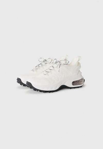 Pair of white low-top sneakers with black-textured laces, black tread soles, and visible air cushioning in the heels.