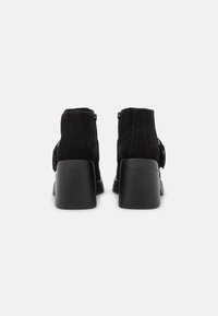 Bottines en suède noir avec un bout arrondi, équipées d'une fermeture éclair au dos et d'un talon bloc. Texture lisse et design minimaliste.