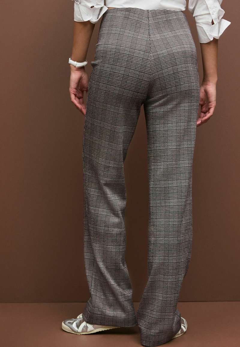 Rudede højtaljede bukser i grå med løs pasform. Stoffet har et lille rutenetmønster. Nederste kant falder lige over skoene og er stylet med loafers.