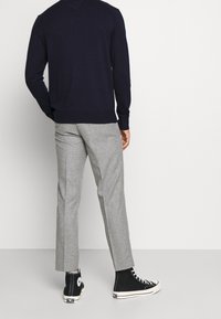 Maglione blu navy, pantaloni grigi su misura e scarpe da ginnastica basse nere. I pantaloni hanno una vestibilità slim e un sottile motivo a spina di pesce.