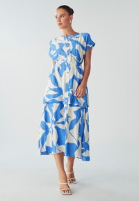 Haljina plave i bijele boje s uzorkom, kratkih rukava, dugmadi sprijeda i višeslojnim dizajnom. Glatka tkanina s lepršavim siluetom.