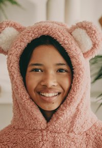 Pinkes Fleece-Hoodie-Decke mit Bärenohren und weißen Akzenten, die eine strukturierte, flauschige Oberfläche hat. Warmes und gemütliches Design.