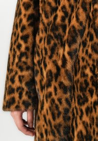 Nærbilde av en hånd ved siden av en brun og svart leopardmønstret faux fur jakkeerm.